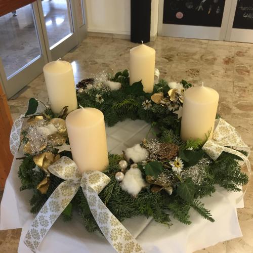 Ein Adventkranz mit weißen Kerzen, weißen Maschen und goldenen Kugeln.