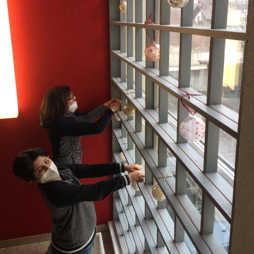 Ein Schüler und eine Lehrperson hängen Weihnachtskugeln ans Fenster.