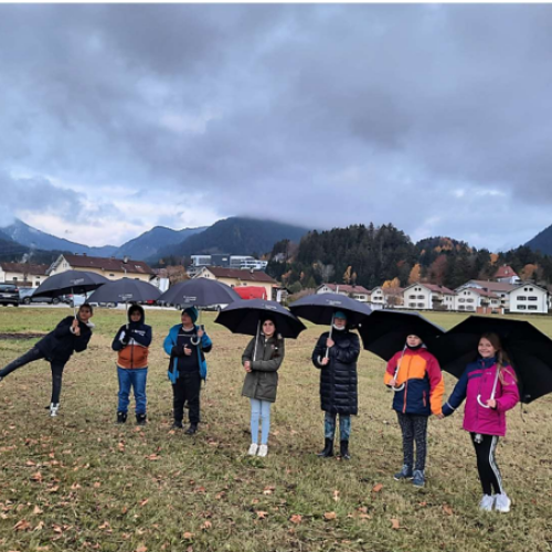 Schülerinnen und Schüler mit schwarzen Regenschirmen in der Wiese.