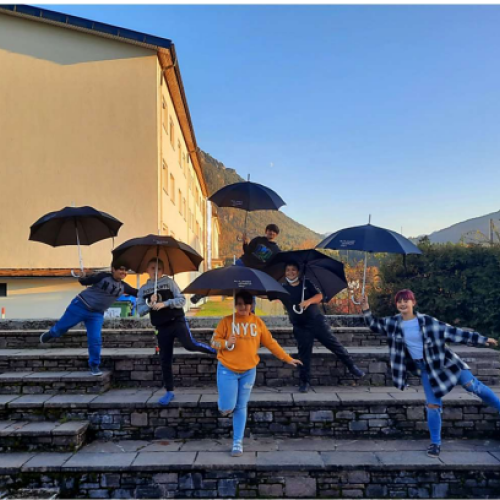 Schülerinnen und Schüler vor der Schule mit schwarzen Regenschirmen in der Hand