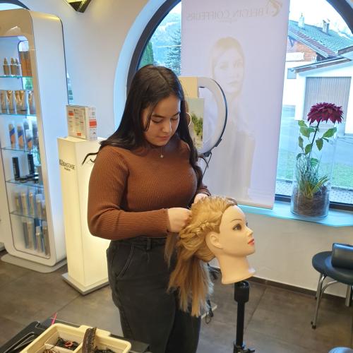 Eine Schülerin übt eine Frisur an einer Puppe.