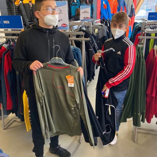 Zwei Schüler in einem Kleidungsgeschäft mit Pullovern in der Hand.
