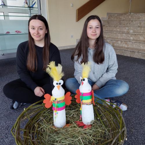 Schülerinnen sitzen vor dem geflochtenen Vogelnest mit den Spaßvögeln.
