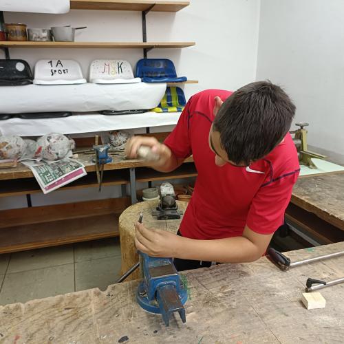 Ein Schüler bearbeitet ein Holzstück mit einem Stein.