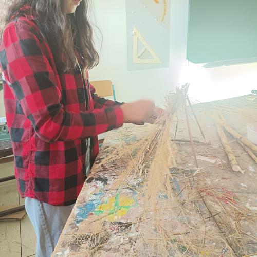 Eine Schülerin baut ein Haus aus Holz und flechtet ein Dach.