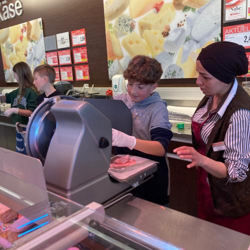 Schüler beim Schneiden von Wurst in der Feinkostabteilung. 