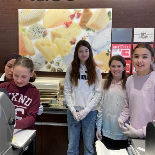 Schüler:innen hinter der Feinkost beim Schneiden von Wurst.