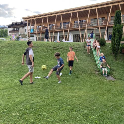 Schüler spielen Fußball. Im Hintergrund sieht man einen Teil der Unterkunft.