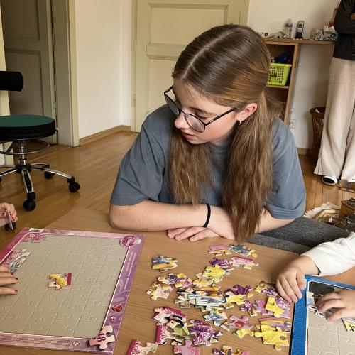 Eine Schülerin löst mit zwei Kindern ein Puzzle.