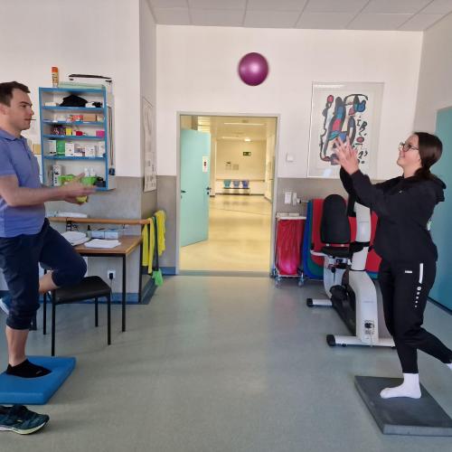 Eine Schülerin macht Übungen mit einem Physiotherapeuten. Sie werfen sich einen Ball zu während sie balancieren.
