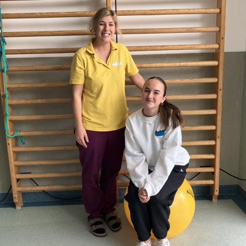Eine Schülerin sitz auf einem gelben Gymnastikball und wird an der Seite einer Physiotherapeutin fotografiert.