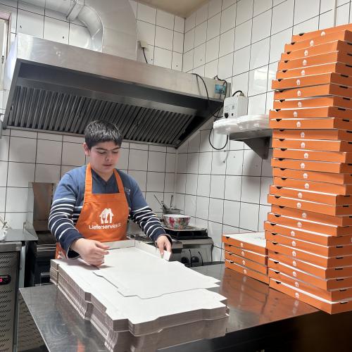 Ein Schüler faltet Pizzakartons in der Küche. 
