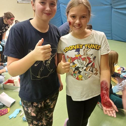 Zwei Schülerinnen zeigen ihre geschminkten Verletzungen. Eine am Arm.