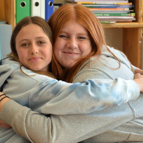 Zwei Mädchen umarmen sich und lachen in die Kamera.