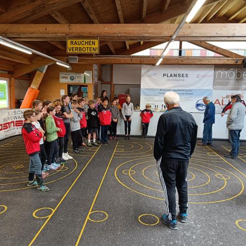 Schüler:innen hören den Erklärungen fürs Stockschießen zu.