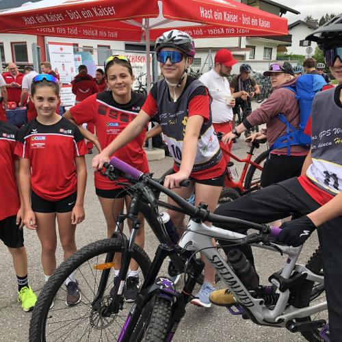 Zwei Schüler sitzen auf dem Fahrrad und drei stehen daneben und lächeln in die Kamera.