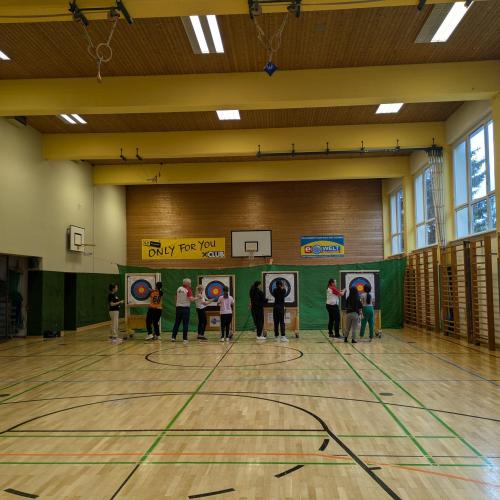Foto im Turnsaal, während die Schülerinnen die Pfeile einsammeln.