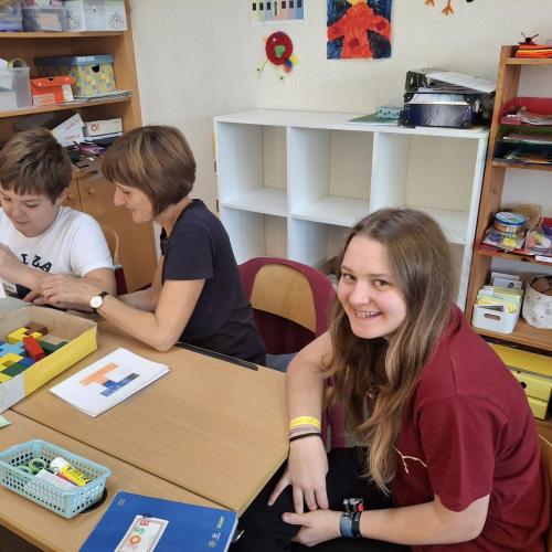 Eine Schüler beim sitzt mit einer Pädagogin und einem Kind am Tisch. 