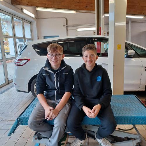 Zwei Schüler sitzen auf einer Hebebühne bei KFZ Lexl.