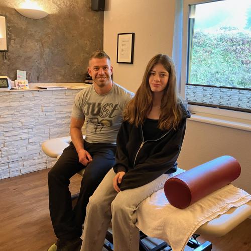 Eine Schülerin sitzt am Massagetisch in einer Physiotherapie.