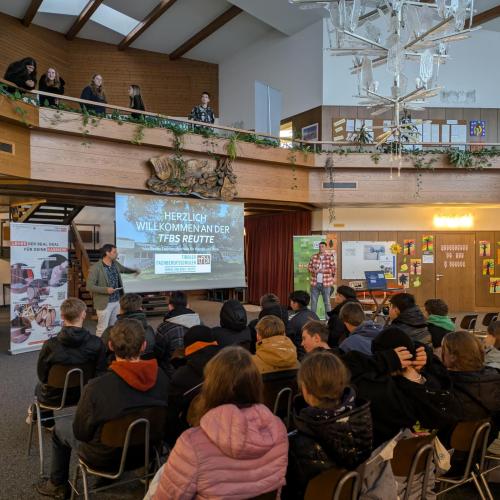 Die Schüler:innen hören dem Direktor beim Kurzvortrag zu.