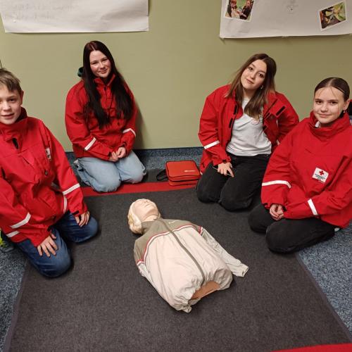 Schüler:innen sitzen bei einer Reanimationspuppe.