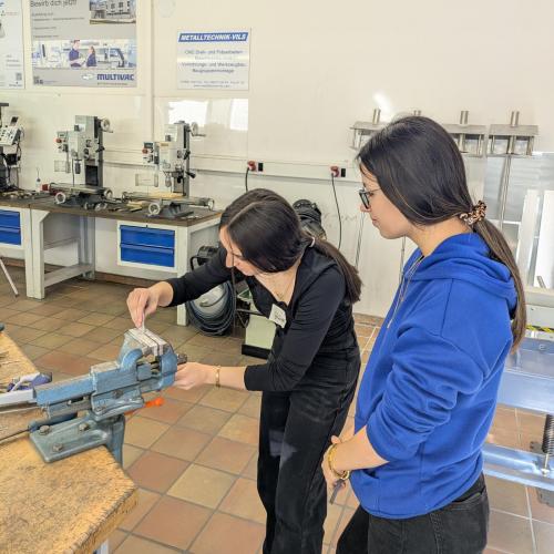 Zwei Schülerinnen bearbeiten ein Metallwerkstück um einen Schlüsselanhänger herzustellen.