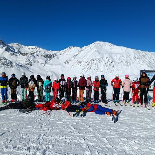 Gruppenfoto bei strahlendem Sonnenschein vor einer schneebedeckten Bergkulisse.