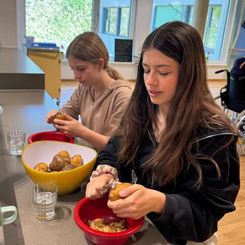 Schülerinnen schälen Kartoffeln.