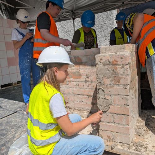 Schülerin verputzt eine Ziegelwand mit Mörtel.