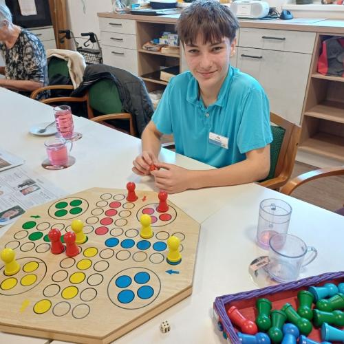 Schüler spielt mit einer Person im Altersheim Mensch-Ärgere-Dich-Nicht