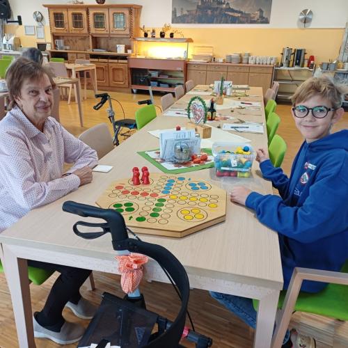 Schüler im Altersheim beim Brettspiel mit einer älteren Dame.