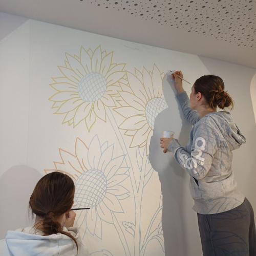 Schülerinnen beim Malen der Blumen. Die Vorlage wird mit einem Overheadprojektor auf die Wand projiziert.