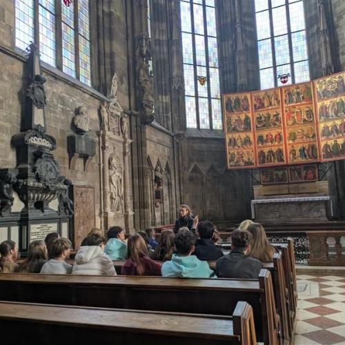 Schüler:innen sitzen in den Bänken im Stephansdom, während eine Frau ihnen spannende Dinge erzählt hat.