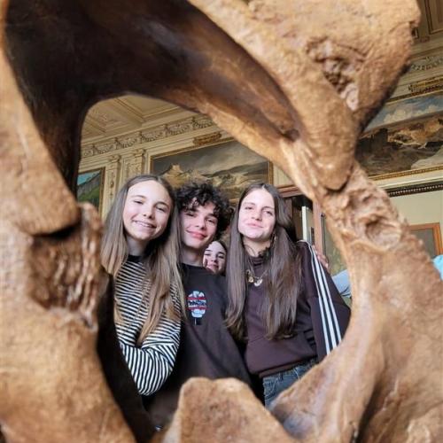 3 Schülerinnen werden durch die Aushölung eines Dinosaurierknochens hindurch fotografiert.