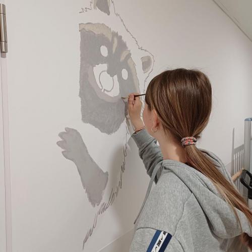 Schülerin malt ein Waldtier auf die Wand.