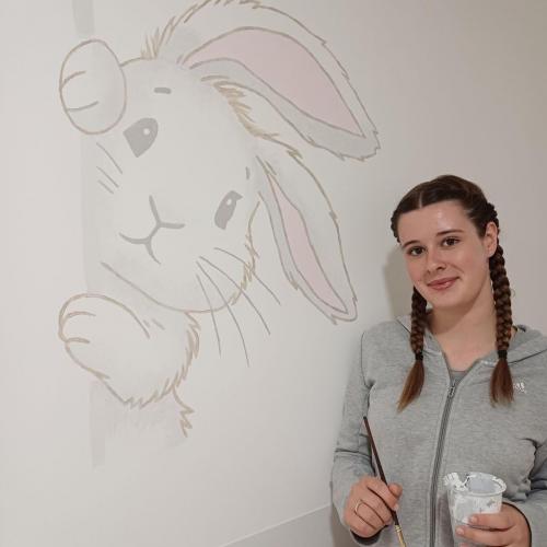 Schülerin malt ein Waldtier auf die Wand.