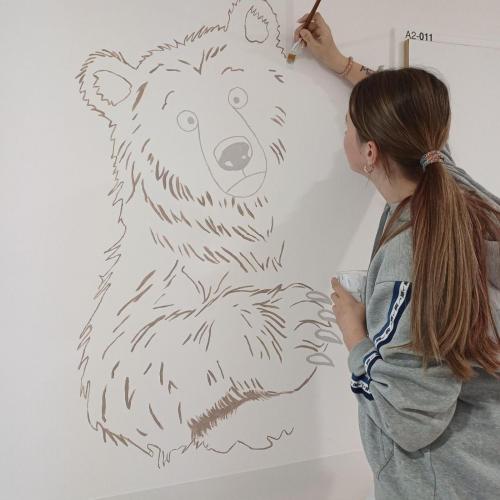 Schülerin malt ein Waldtier auf die Wand.