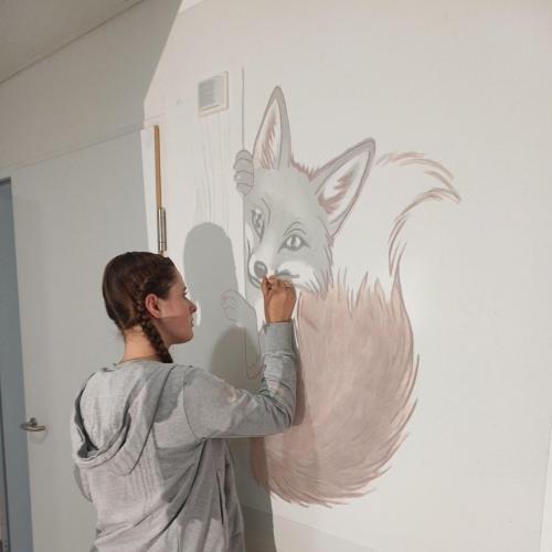 Schülerin malt ein Waldtier auf die Wand.