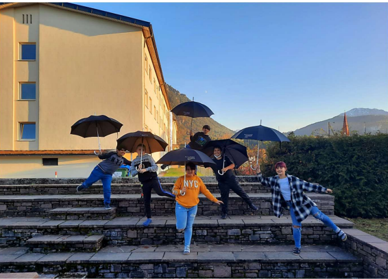 Schülerinnen und Schüler vor der Schule mit schwarzen Regenschirmen in der Hand