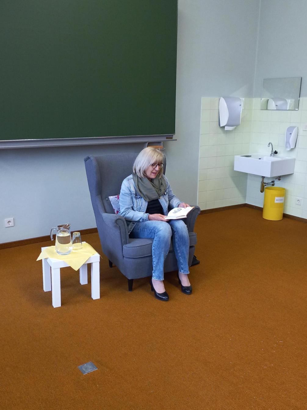 Frau Dr. Beate Palfrader sitzt in einem Sessel und liest vor.