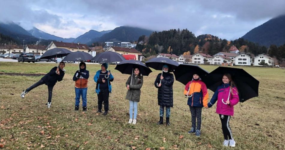 Schülerinnen und Schüler mit schwarzen Regenschirmen in einer Wiese