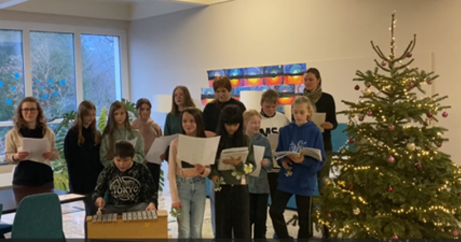 Schüler:innen und Lehrpersonen vor dem Tannenbaum der Schule singen Jingle Bells auf Italienisch und Französisch.