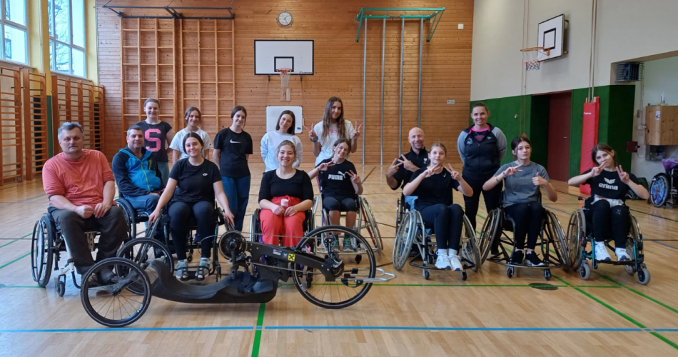 Gruppenfoto im Turnsaal. Die Schüler:innen sitzen im Rollstuhl, um zu erleben, was dies bedeutet.