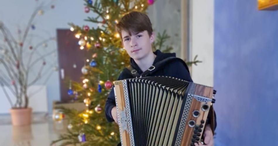 Schüler sitzt mit einer Ziehharmonika vor dem Weihnachtsbaum der Schule.
