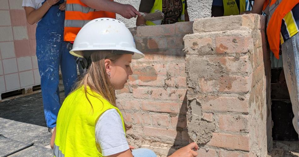 Schülerin verputzt eine Ziegelwand mit Mörtel.