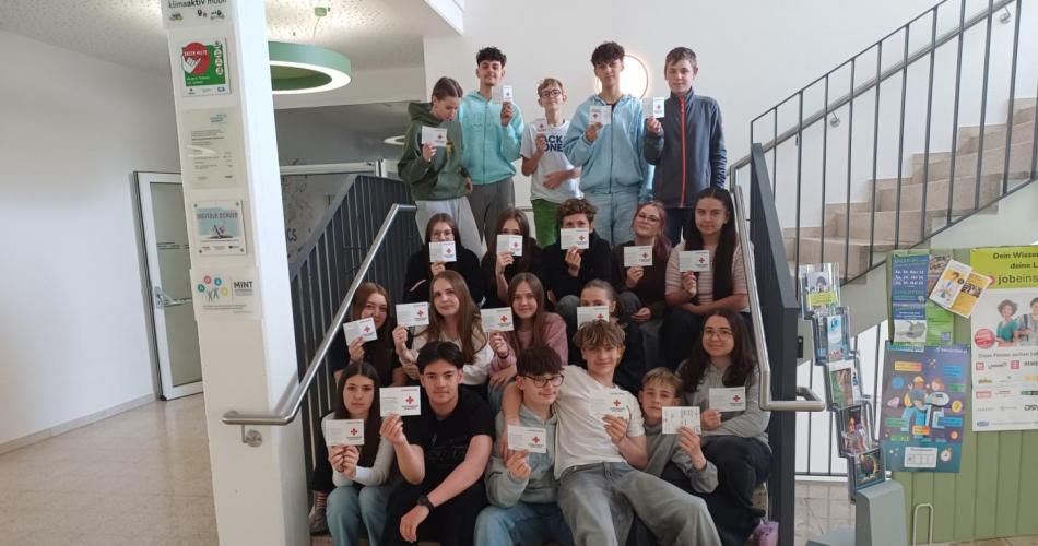 Klasse 4c sitzt auf den Stiegen und hält stolz ihre Erste Hilfe Scheine in die Kamera.
