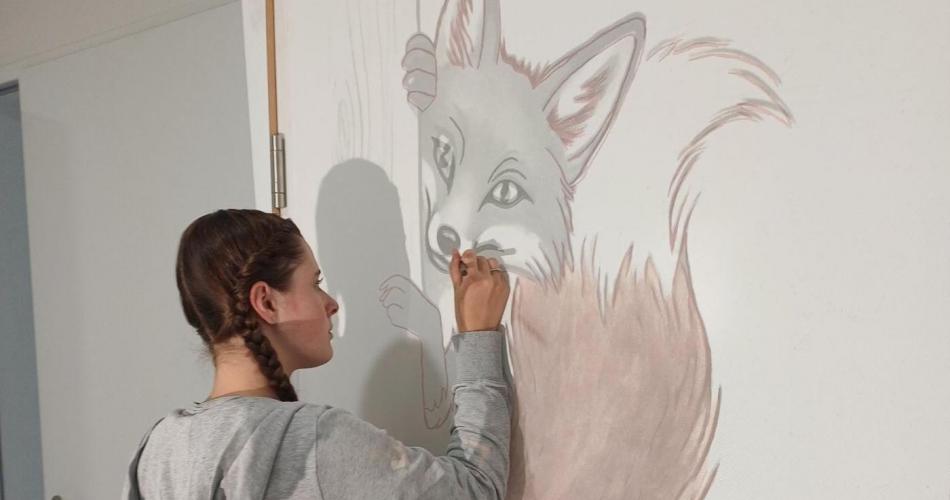 Schülerin malt ein Waldtier auf die Wand.